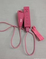 Pink Wii Remote controller with matching Nunchuk attachment and wrist strap laid out on flat surface.