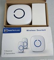 Photo of the wireless doorbell receiver and transmitters in an open box with the product packaging showing the brand and item details.