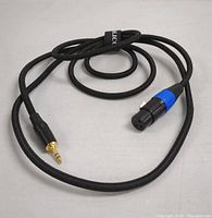 Black audio cable with one female XLR connector and one gold-plated 3.5mm male connector. Cable is braided and coiled with a Velcro strap.