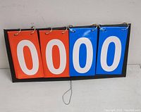 Front view of the sports scoreboard showing four large flip cards displaying '0000' with two red and two blue cards attached to a black base.