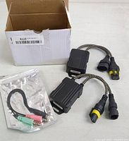 Photo showing one black rectangular anti-flicker Canbus module with braided wire and sealed connectors, white box, and accessory wiring adapter in plastic bag.