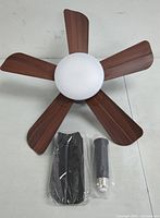 Top view of ceiling fan showing five wooden blades and central white dome light, alongside mounting rod and black component.