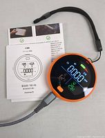 Top-down photo of Gedsffati carbon monoxide detector showing digital screen with readings and user manual underneath, accompanied by a black wrist strap lanyard.