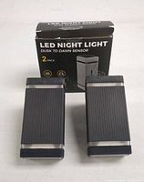 Two black LED night lights with dusk to dawn sensor standing upright with packaging box behind