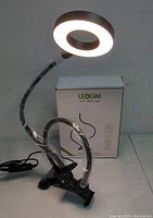 LEDGIE 2-in-1 Ring Light powered on, showing illuminated ring light with flexible arm and clamp base attached to surface.