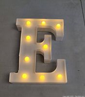 Front view of illuminated letter E standee showing warm yellow LED lights powered on, displaying good glow.