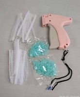 Pink plastic tagging gun, white plastic fastener strips, and two bags of blue plastic fasteners laid out on a flat surface.