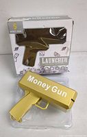Gold plastic money gun toy labeled 'Money Gun' with its packaging box