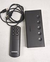 Top view of Ugreen HDMI switch with remote control and USB power cable showing front buttons and branding.