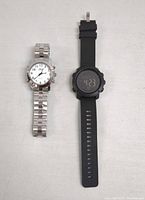 Two wristwatches displayed: one analog with silver metal band and white dial, one black digital with rubber strap
