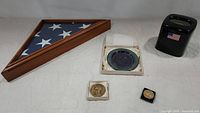 Full view of all items: folded American service memorial flag in wooden display case, Dwight D. Eisenhower silver dish in box, tissue box cover with American flag, Eisenhower gold coin, and Reagan gold coin.