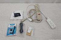 Photo of all items in the lot including Samsung SSD box, USB WiFi adapter in package, power strips, cords, and package of domino-shaped USB flash drives.