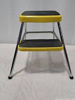 Front angled view of the yellow Cosco Stylair step stool showing rubber treads and chrome legs.