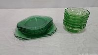 Grouped image showing two stacks: seven square Mayfair plates on left, eight scalloped berry bowls on right, all green uranium glass.