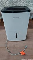 Front view of white Frigidaire dehumidifier showing water level indicator and power cord with plug.