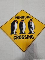 Full view of the yellow diamond-shaped metal sign with three penguins and 'Penguin Crossing' text.