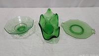 Three green uranium glass items displayed side-by-side on white background: pedestal etched serving plate, dolphin handled bonbon dish, octagon etched serving plate.