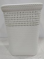 Front view of the white plastic rattan style hamper showing the tight weave at the bottom and a more open pattern near the top with the fitted lid.