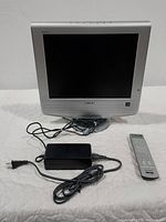 Front view of the silver Sony WEGA TV with the screen turned off, showing the included remote control and power adapter with cord lying in front of it.