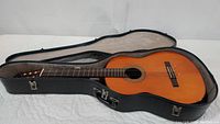 Yamaha acoustic guitar placed open in its black hard case showing the natural wood guitar body and rosewood fingerboard