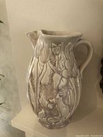 Front angle showing detailed squirrel and fox raised figures within forest motif on cream ceramic jug.
