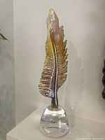 Full view of the amber and brown lead crystal glass feather sculpture with clear base.