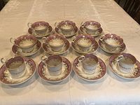 Full view of 7 tea cups and 4 coffee cups with matching saucers arranged on table.