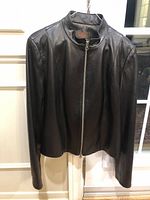 Front view of the dark brown leather jacket hanging, showing the full front zipper and collar design.