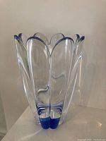 Front side view of a clear crystal vase with blue edges on the petal-shaped rim and base, standing on a flat surface.