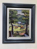 Framed painting hanging on wall, showing full view of black carved frame with white liner and landscape image