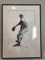 Full view of framed watercolor painting of Toronto Blue Jays player pitching, showing entire artwork and frame.