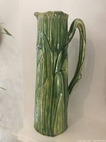 Front and side views of the green tulip-shaped ceramic jug showing detailed leaf and twig handle design with matte green glaze.