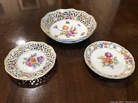 Set of three Schumann Bavaria Dresden porcelain candy plates on wood surface, showing variation in size and floral designs