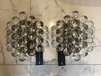 Two sconces side by side on a marble floor showing full front profiles and glass sphere clusters