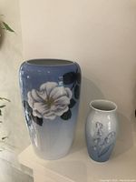 Two porcelain decorative vases placed on a white surface, one larger with white flower on blue background and smaller with blue floral pattern.
