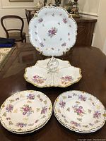 Front view of the set including large handled serving dish, 3-compartment divided dish with handle, and four smaller plates all decorated with floral patterns and gold edging.