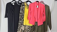 Full view of all five clothing items hung on hangers showing different colors and styles including black, leopard print, yellow, coral pink, and olive green.