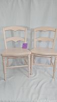 Front view of two light pink wooden children's chairs showing turned legs and horizontal slatted back.