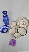 Lot overview showing porcelain plates, teacups with saucers, bowls, and cobalt blue cut glass vase.