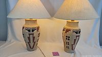 Pair of large table lamps with ceramic bases, geometric Southwestern style patterns in red, black, and blue, cream background, off-white fabric shades, standing approximately 27 inches tall.