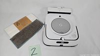 White iRobot Braava Jet robot mop with cleaning pads next to it and a number card '2'