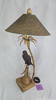 Full view of the lamp showing bamboo-style gold metal base, parrot figure, and conical parchment shade.