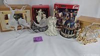 Full view of six assorted Christmas decorative items including glass sleighs with reindeer, angels, and a musical carousel figurine with original boxes.