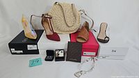 Photo showing four pairs of women's shoes in size 8 from various brands and styles arranged in front of their boxes. Includes a straw crossbody purse, jewelry boxes, wallet and chain bracelet.