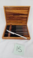 Full view of six steak knives neatly arranged inside an open wooden case, one knife placed diagonally outside the case.