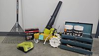 Wide-angle photo showing Ryobi cordless blower, Fiskars rake, lawn watering tractor, toolbox with tools and wipe towels