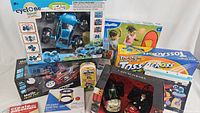 Photo showing full lot including remote control car, Toss Across game, inflatable basketball hoop, FAO Schwarz toy, Kiddozie kit, and Dog Man card game in original packaging