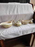 Overall view of the four-piece ceramic set including creamer, sugar bowl with lid, gravy boat, and milk pitcher displayed on white fabric.