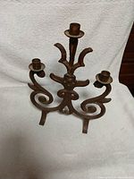 Front view of antique heavy cast iron candle holder showing three candle cups and ornate swirling arms with floral motif on the central stem.