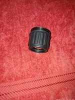 Close-up image of a small black cylindrical night vision optic lens magnifier on a red cloth surface.